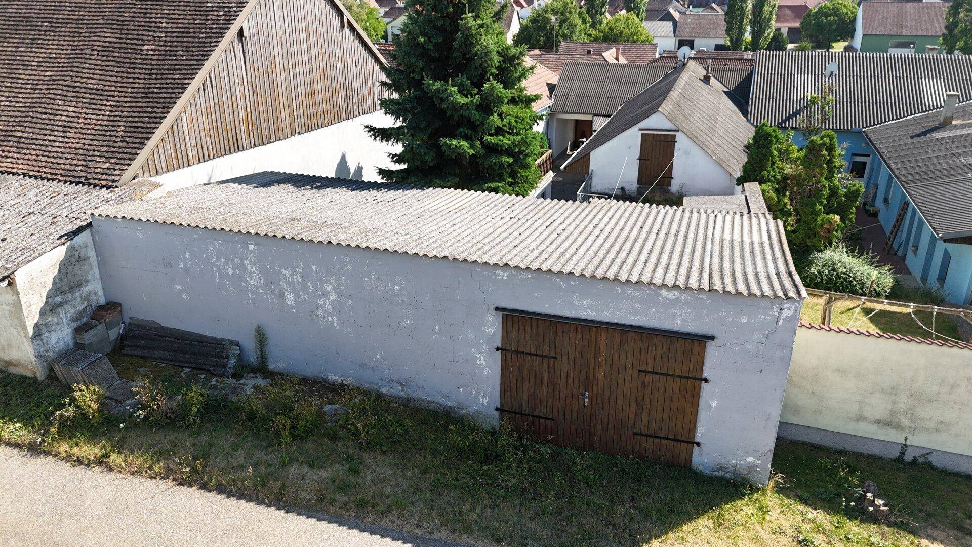 Langes Nebengebäude mit Holztüren und Wellblechdach, umgeben von Gras und einem Weg.