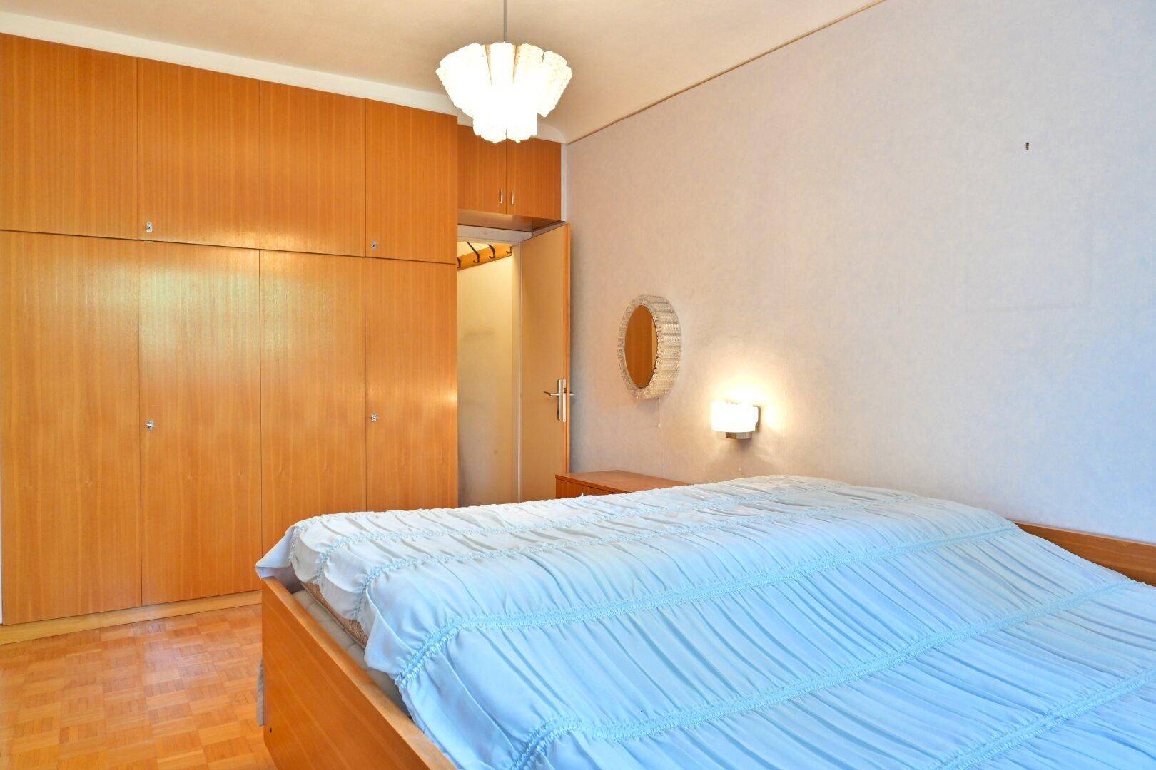 Schlafzimmer mit großem Einbauschrank aus Holz, Doppelbett und Parkettboden.
