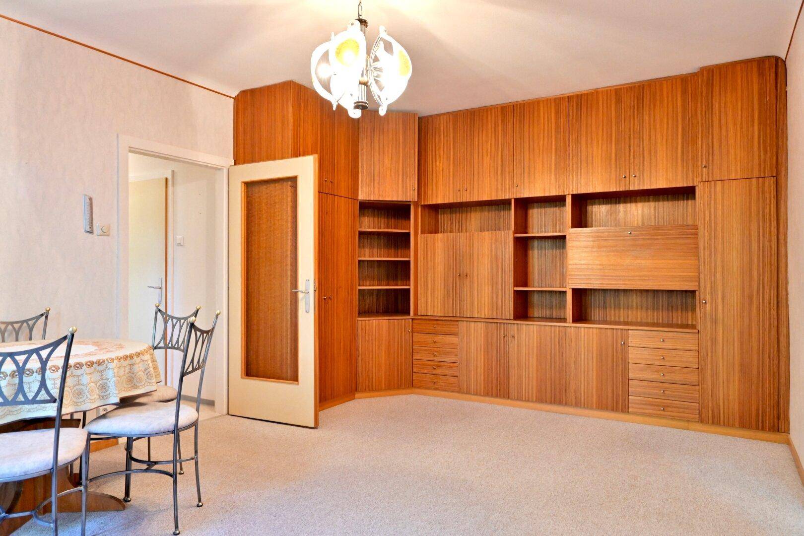 Wohn-Essbereich mit umfangreicher Holz-Wohnwand, Esstisch und Teppichboden.