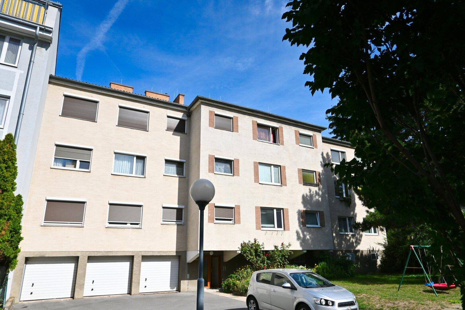 Mehrfamilienhaus mit Garagen, Spielplatz und Grünflächen in sonniger Umgebung.