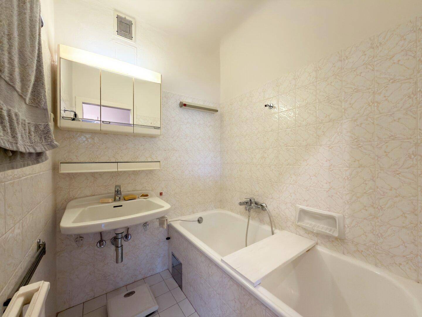 Badezimmer mit Badewanne, Waschbecken, Spiegelschrank und hellen Fliesen.
