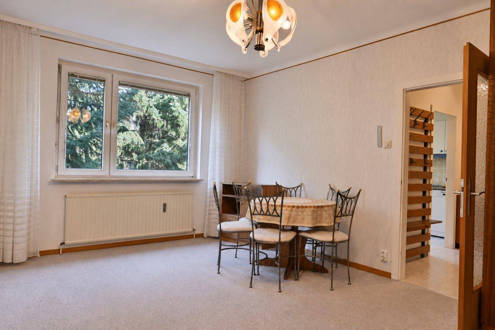 Geräumiger Wohn-Essbereich mit Teppichboden, Esstisch und großem Fenster mit Grünblick.