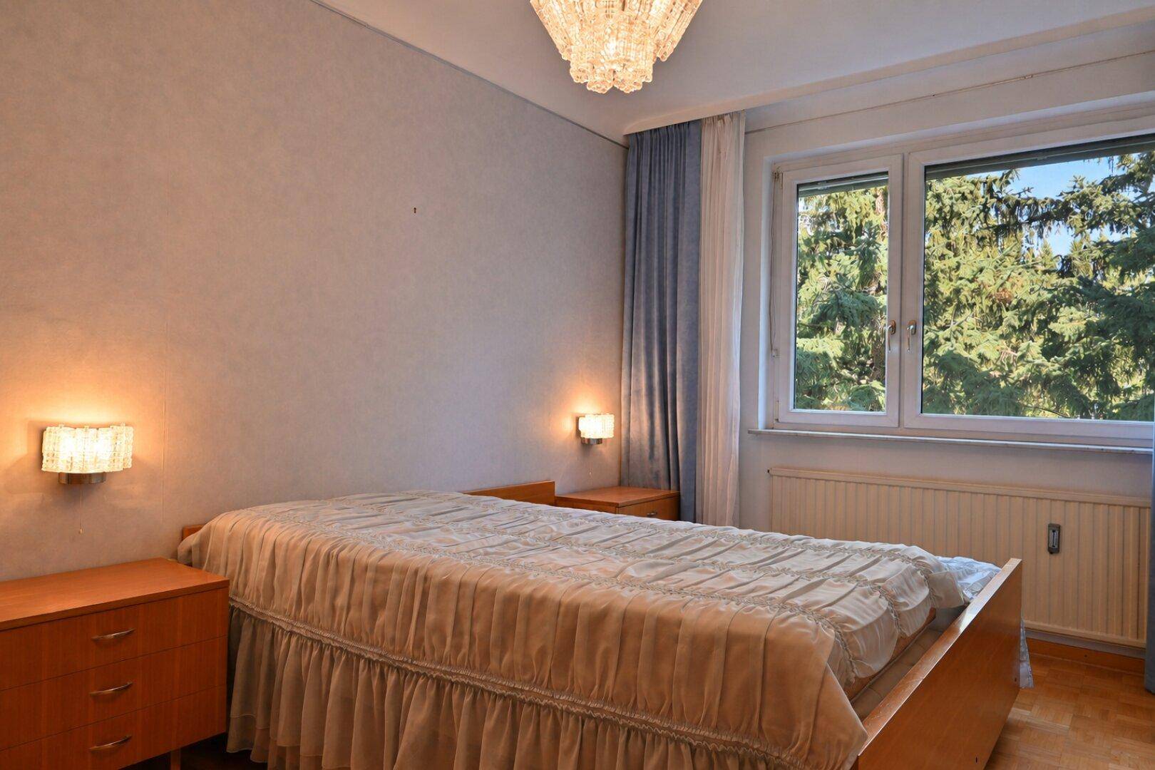 Schlafzimmer mit Einzelbett, Nachttischen und Fenster mit Blick ins Grüne.