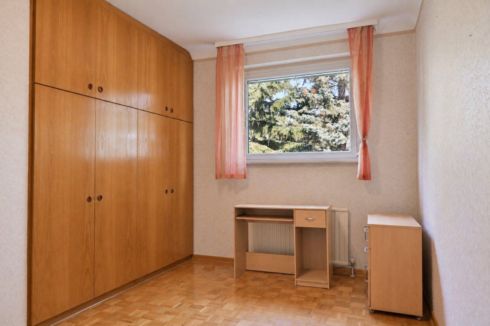 Helles Zimmer mit großem Einbauschrank, Schreibtisch und Fenster.