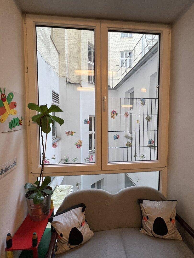 Gemütlicher Fensterbereich mit Sitzgelegenheit und Pflanzen, blickt auf einen ruhigen Innenhof.