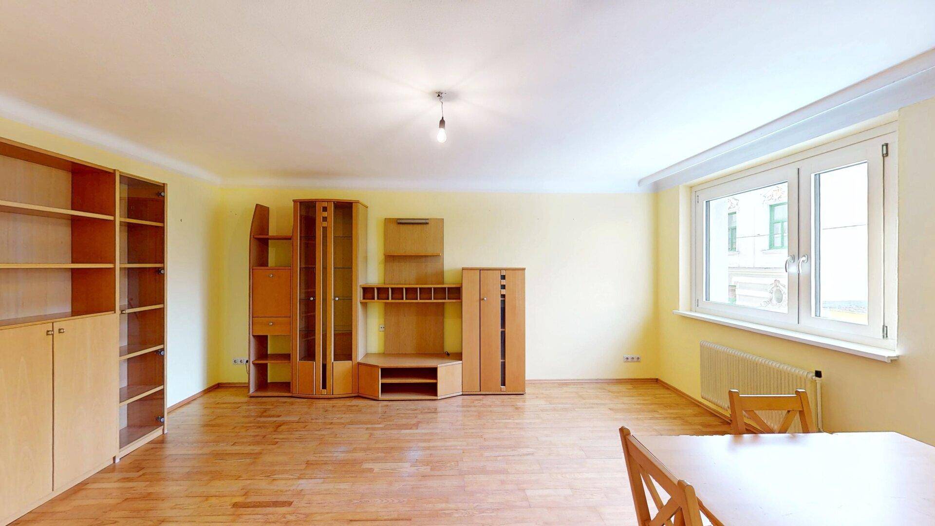 Heller Wohn-Essbereich mit Parkettboden, gelben Wänden und einem großen Fenster.
