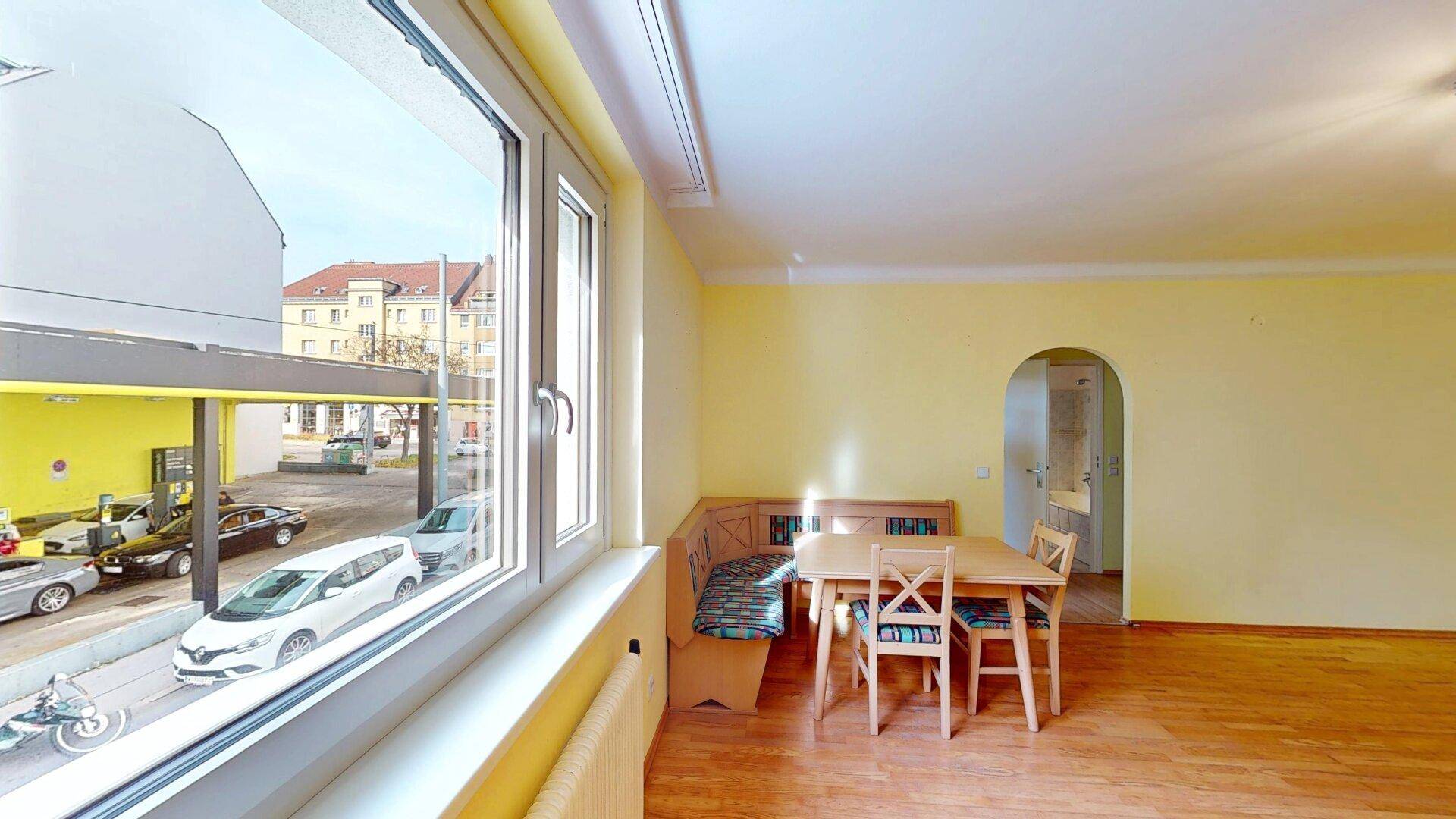 Wohn-Essbereich mit Holztisch und Bank, Blick aus dem Fenster auf die Straße.