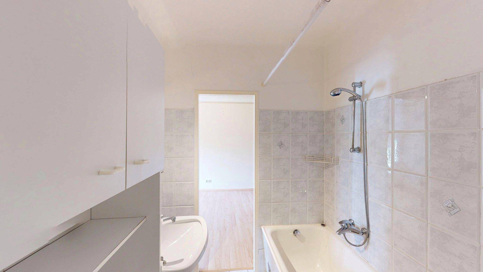 Badezimmer mit Badewanne, Waschbecken und weißen Fliesen, gut beleuchtet.