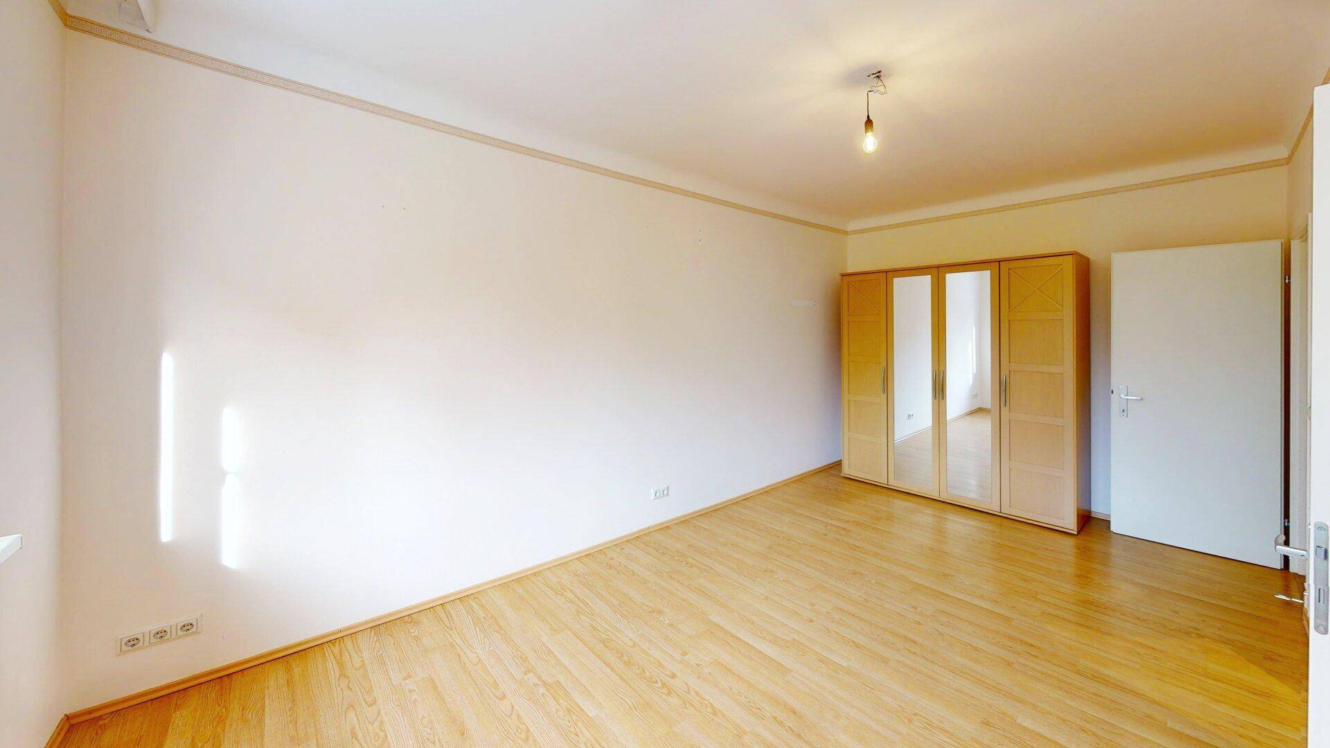 Schlafzimmer mit Parkettboden, weiß gestrichenen Wänden und einem Kleiderschrank mit Spiegeltüren.