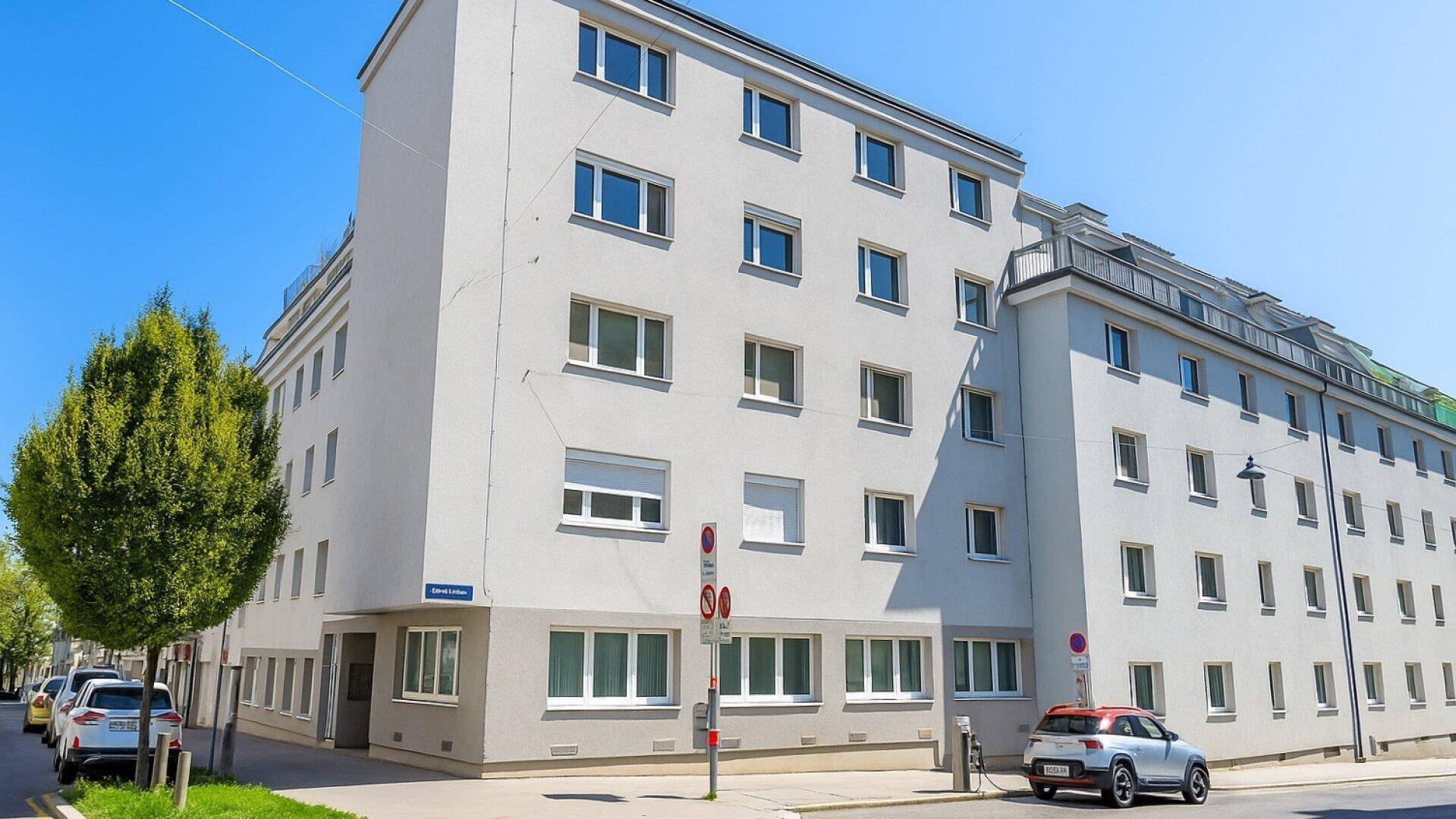 Ansicht eines modernen Wohngebäudes mit vielen Fenstern und einem Baum im Vordergrund.