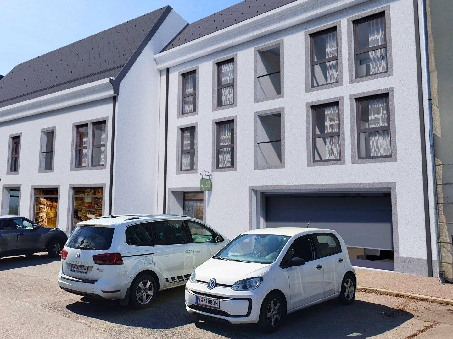 Weißes Gebäude mit grauen Fensterrahmen und Garagentor, davor parken zwei Autos.