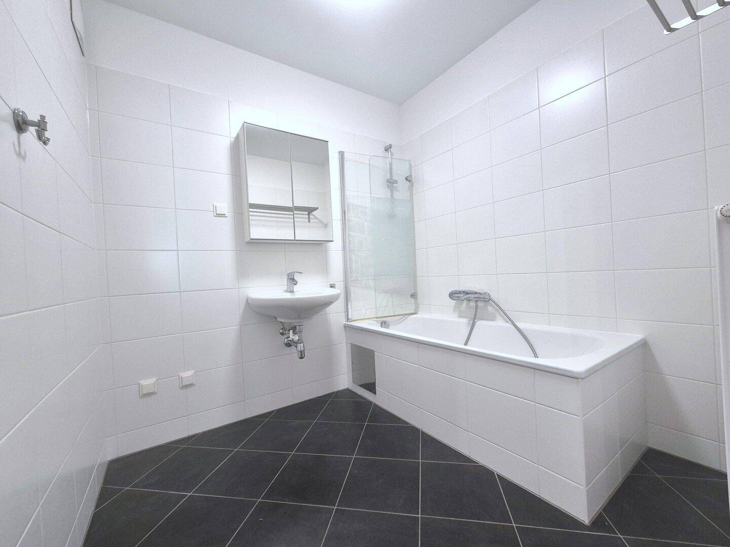 Modernes Badezimmer mit Badewanne, Duschabtrennung und weißen Wandfliesen.