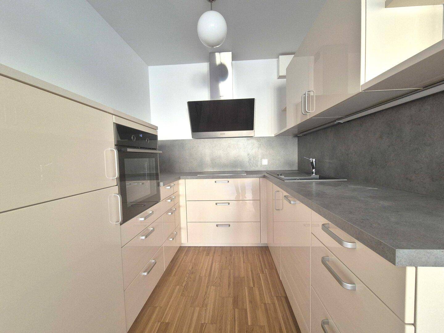 Moderne Küche mit hellen Hochglanzfronten, integriertem Backofen und Dunstabzugshaube.