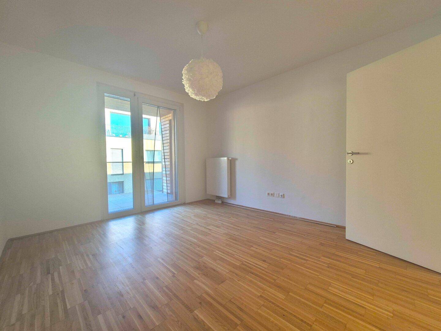 Helles Schlafzimmer mit Holzboden und großem Fenster zum Außenbereich.