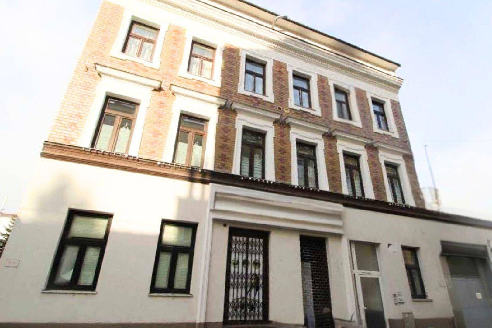 Historisches Mehrfamilienhaus mit klassischer Fassade, vielen Fenstern und Ziegelmauerwerk in den oberen Etagen.