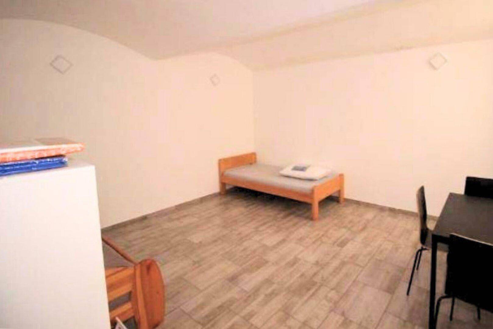 Schlichtes Schlafzimmer mit Einzelbett, kleinem Tisch und hellen Fliesenböden, ideal als Gästezimmer.