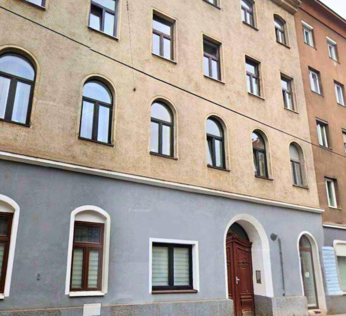 Historische Fassade eines Mehrfamilienhauses mit verschiedenen Fensterformen und einem Holztor im Stadtgebiet.