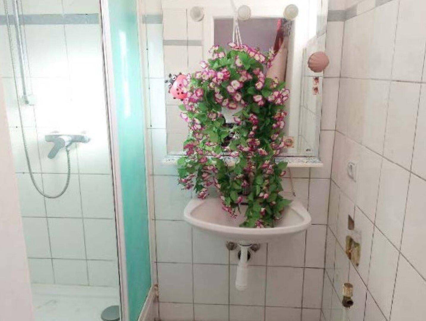 Kleines Badezimmer mit Duschkabine, Waschbecken und weißen Fliesen, typisch für die 80er Jahre.