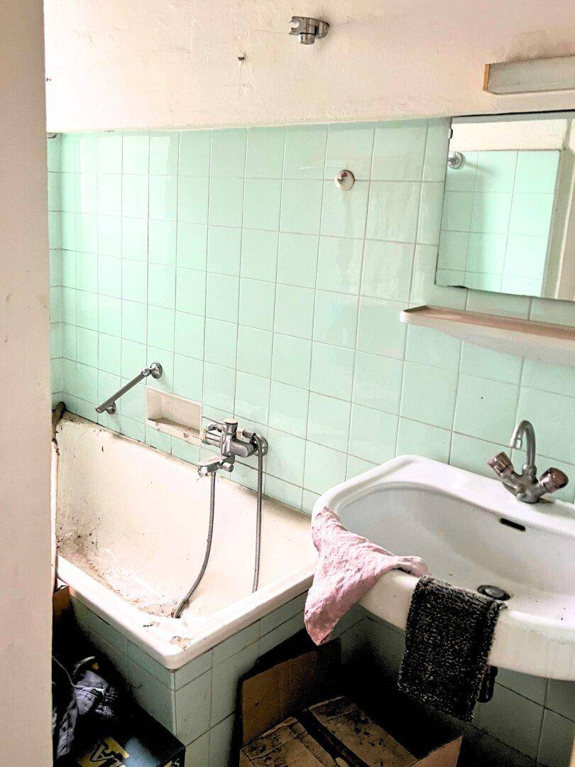Veraltetes Badezimmer mit mintgrünen Fliesen, Badewanne und Waschbecken, renovierungsbedürftig.