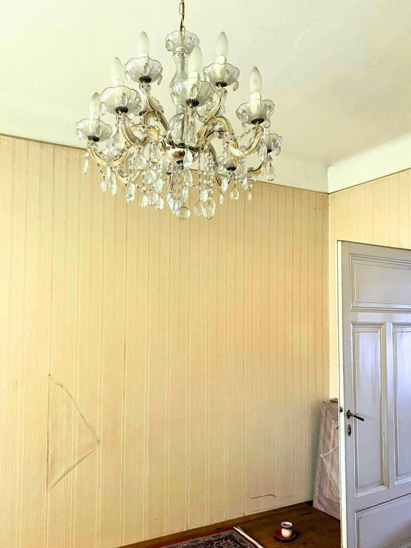 Hoher Raum mit elegantem Kronleuchter, gestreifter Tapete und einer alten Holztür.