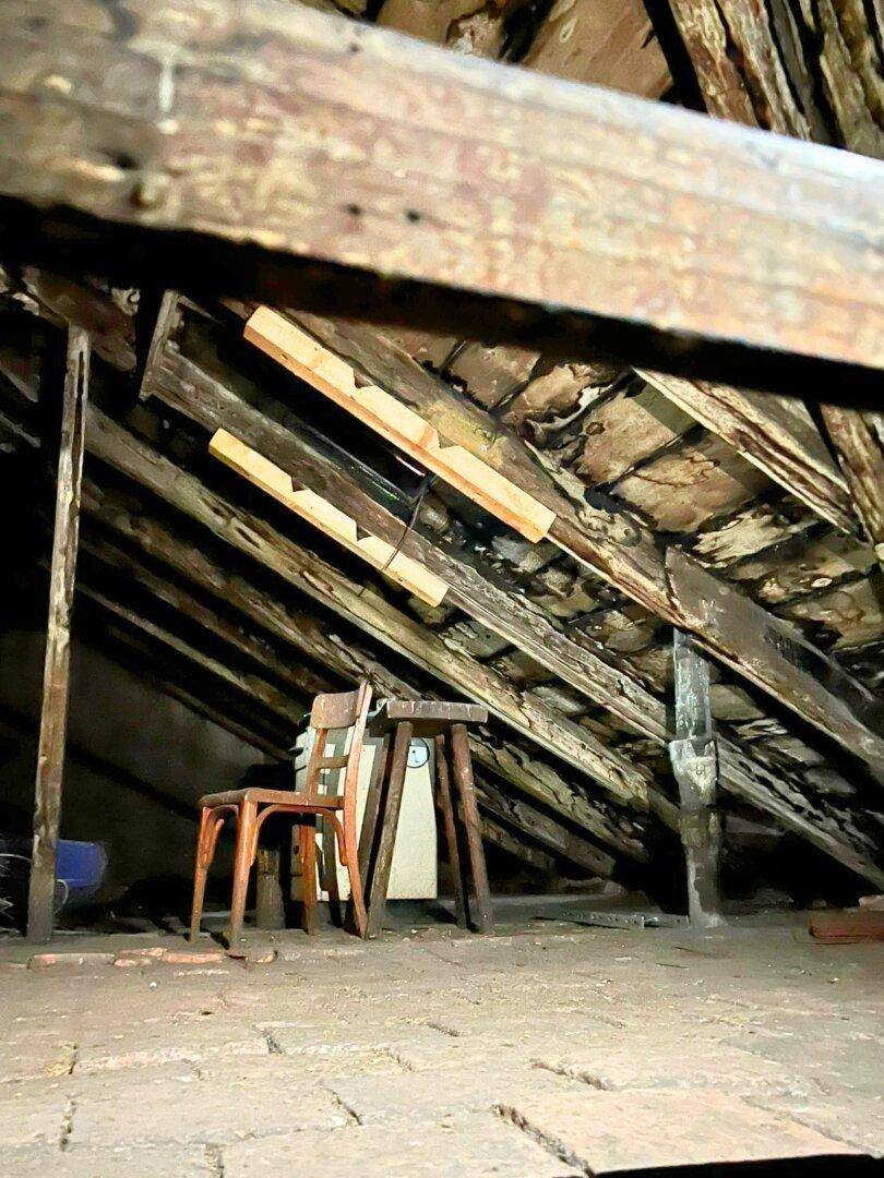 Dachboden mit sichtbaren Holzbalken und schräger Dachkonstruktion, als Lagerraum genutzt.