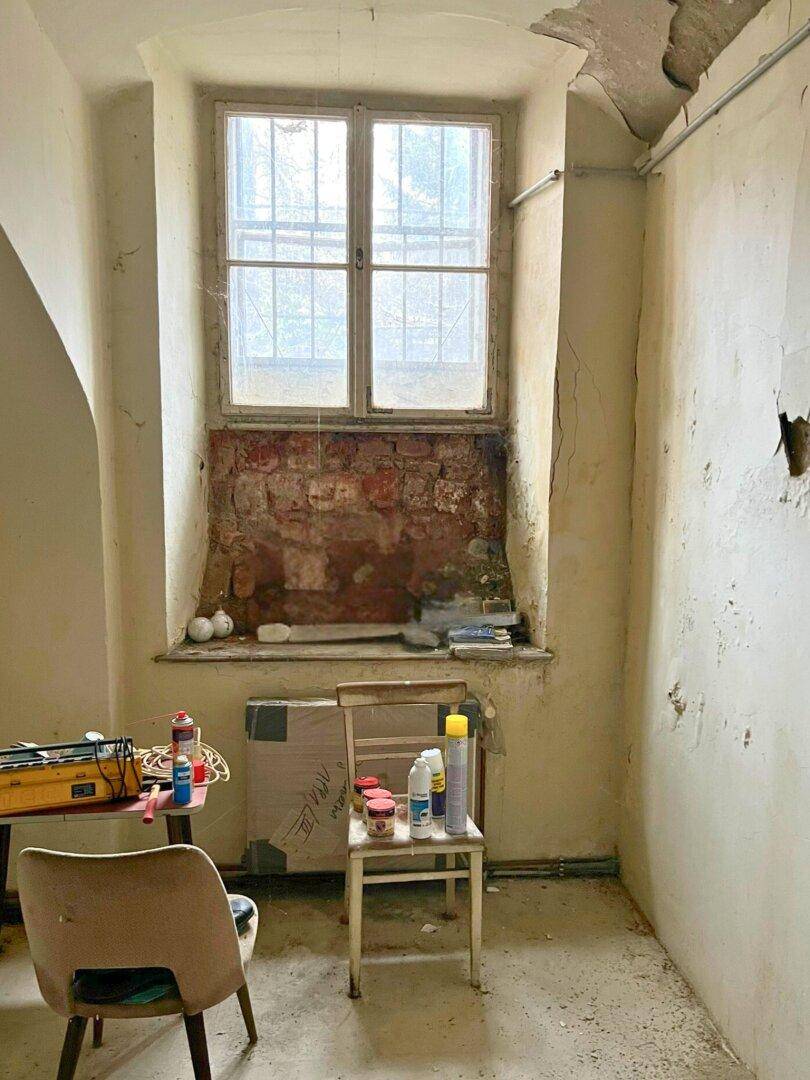 Renovierungsbedürftiger Raum mit altem Fenster, freigelegtem Mauerwerk und unfertigen Wänden.