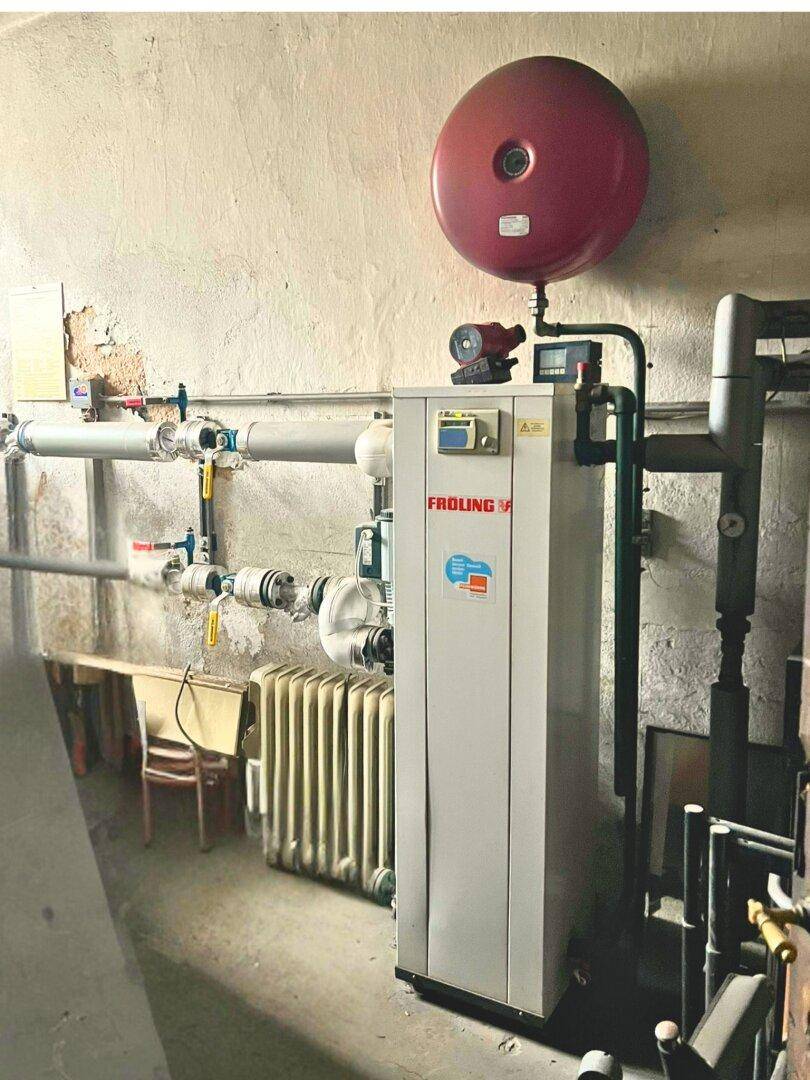 Heizungsraum mit einem modernen Heizkessel und Rohrsystemen, in einem Kellerbereich.
