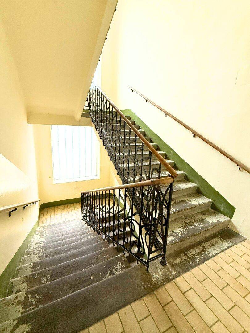 Treppenhaus in einem Altbau mit schmiedeeisernem Geländer und Fliesenboden.