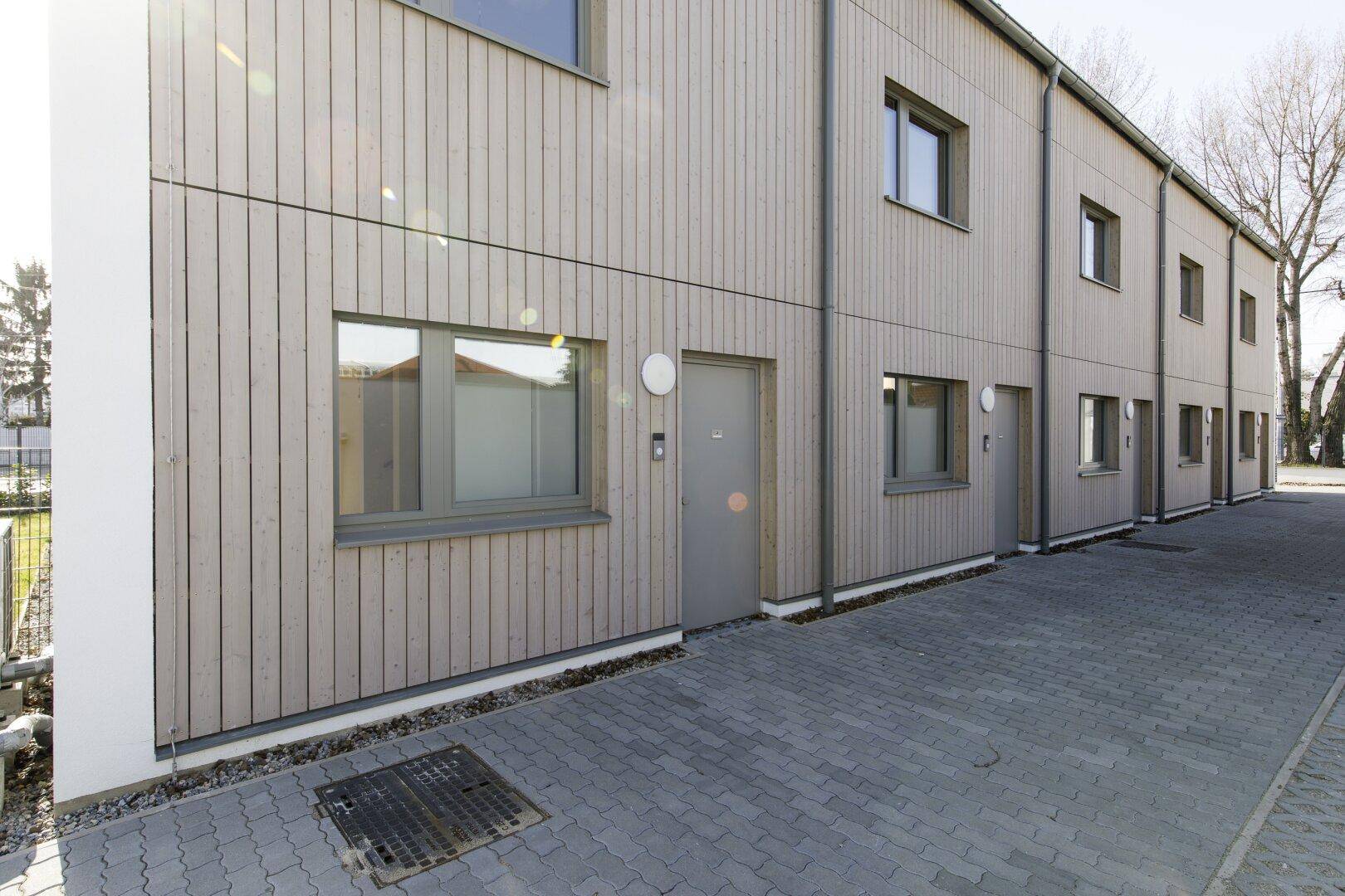 Seitenansicht der Reihenhäuser mit gepflastertem Zugang und Holzelementen.