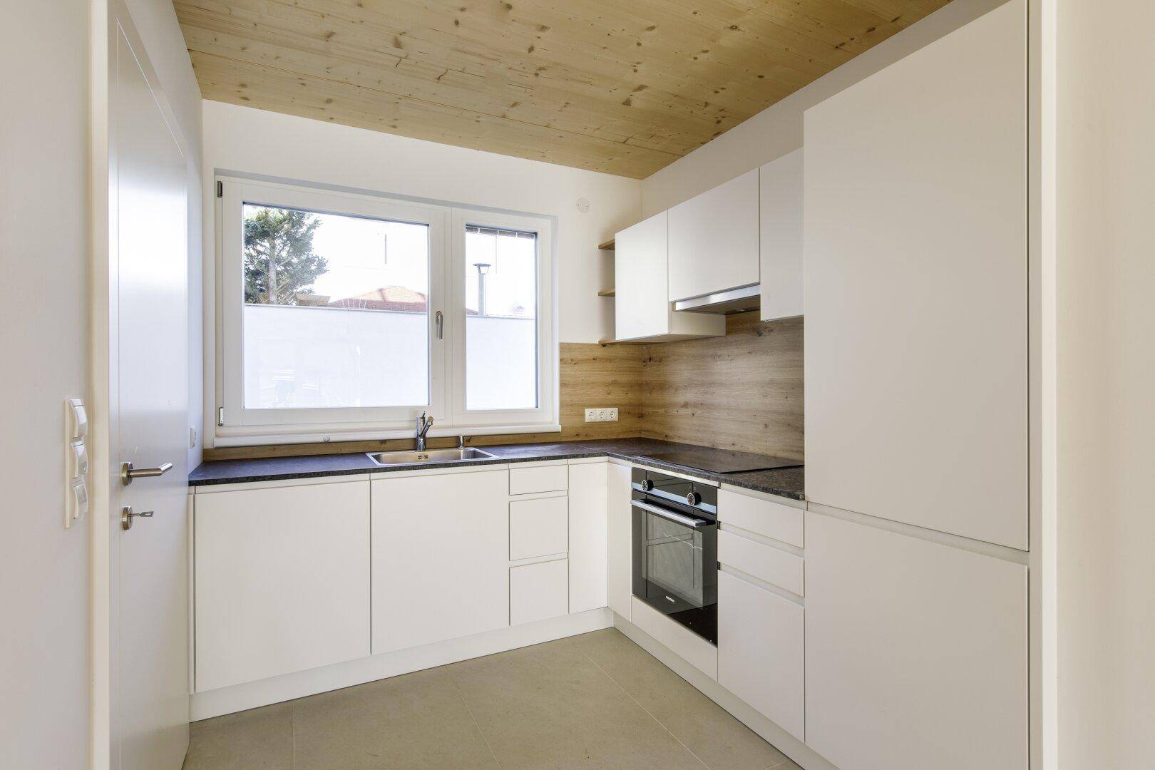 Moderne Einbauküche mit weißen Schränken, dunkler Arbeitsplatte und Holzdecke.