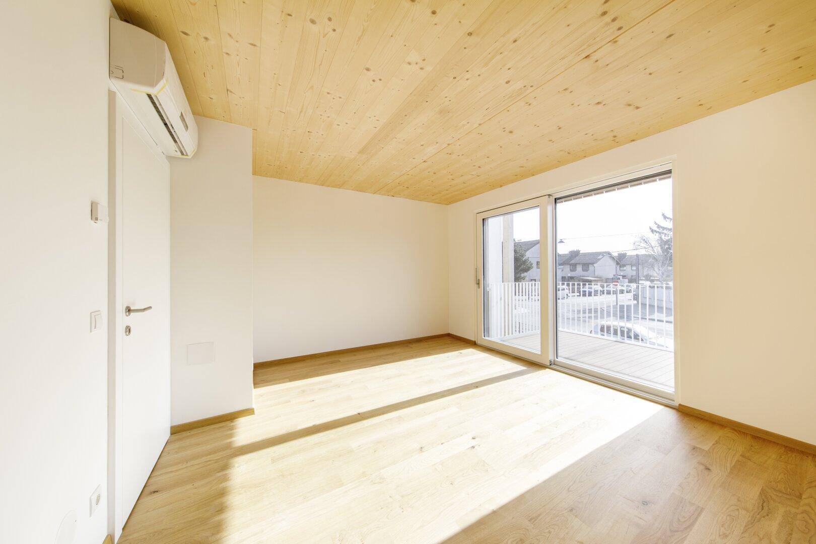 Helles Schlafzimmer mit Holzboden, Holzdecke und Zugang zum Balkon.