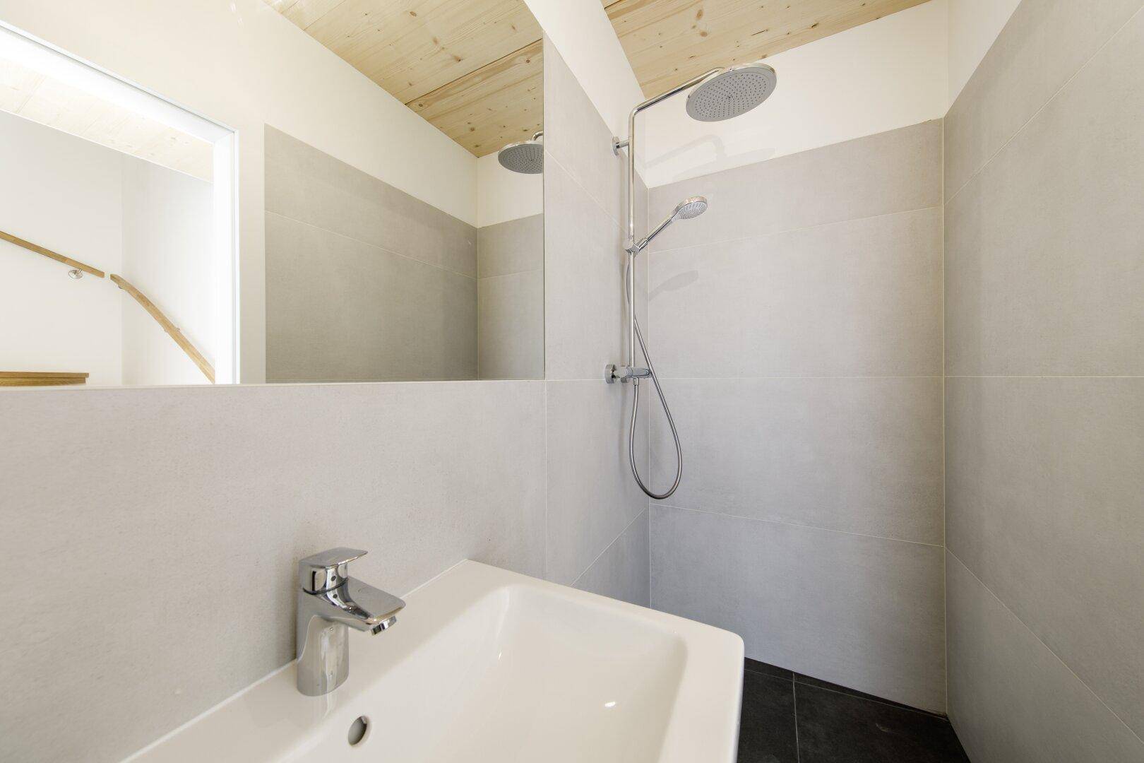 Modernes Badezimmer mit Dusche, Waschbecken und hellen Fliesen.