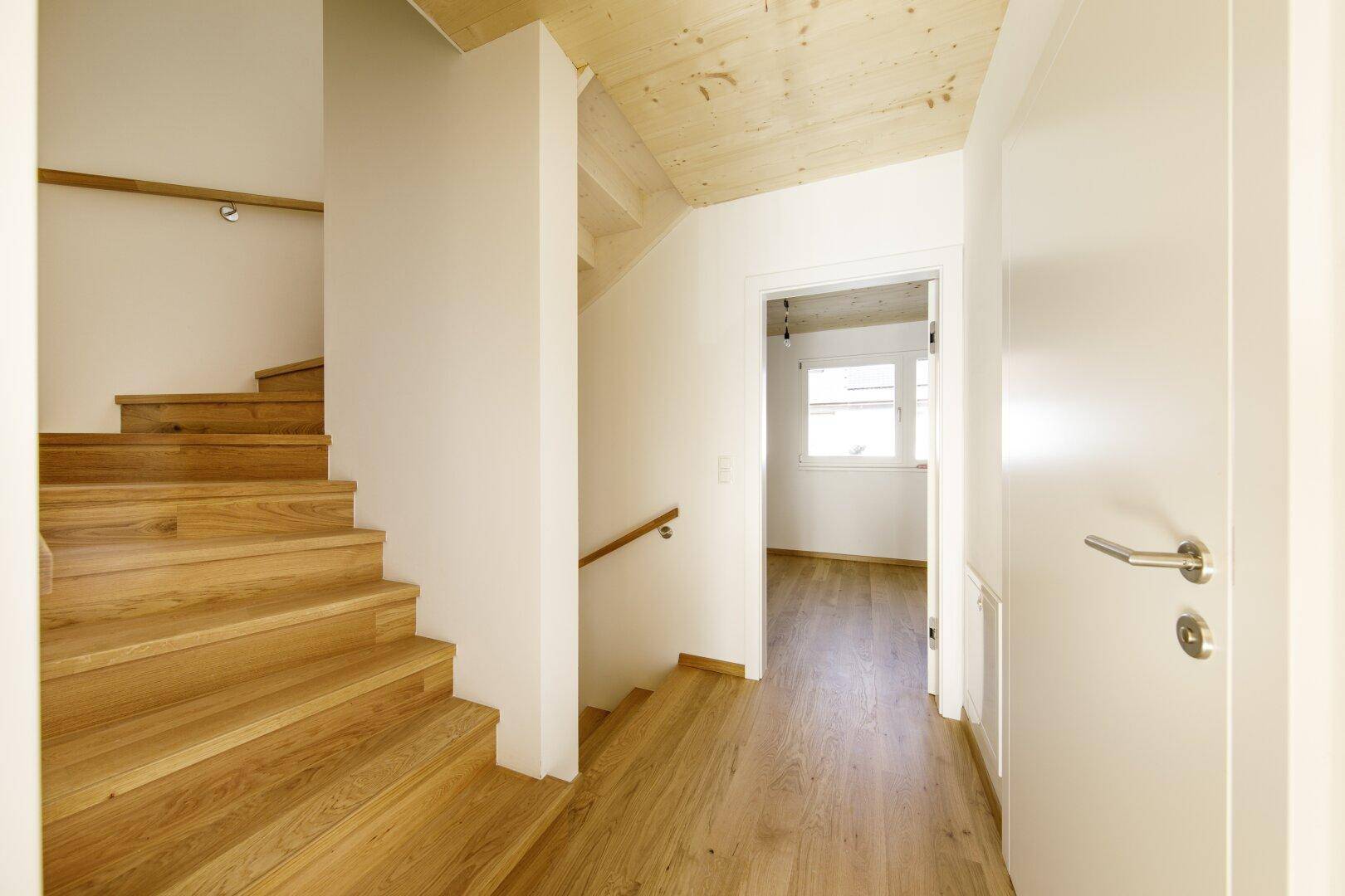 Heller Flur mit Holztreppe und Holzboden, der zu weiteren Räumen führt.