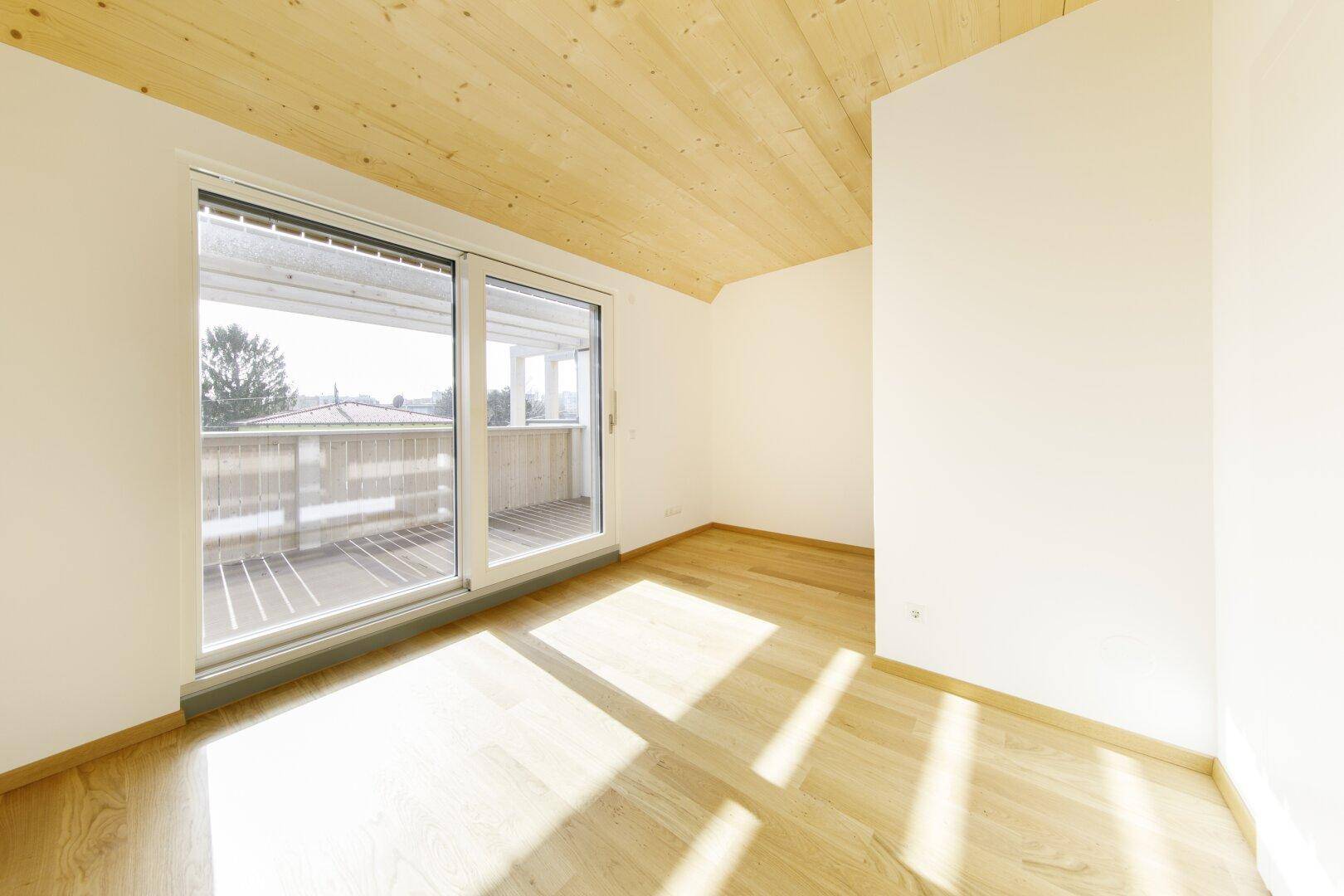 Helles Schlafzimmer im Dachgeschoss mit Holzboden und Balkonzugang.