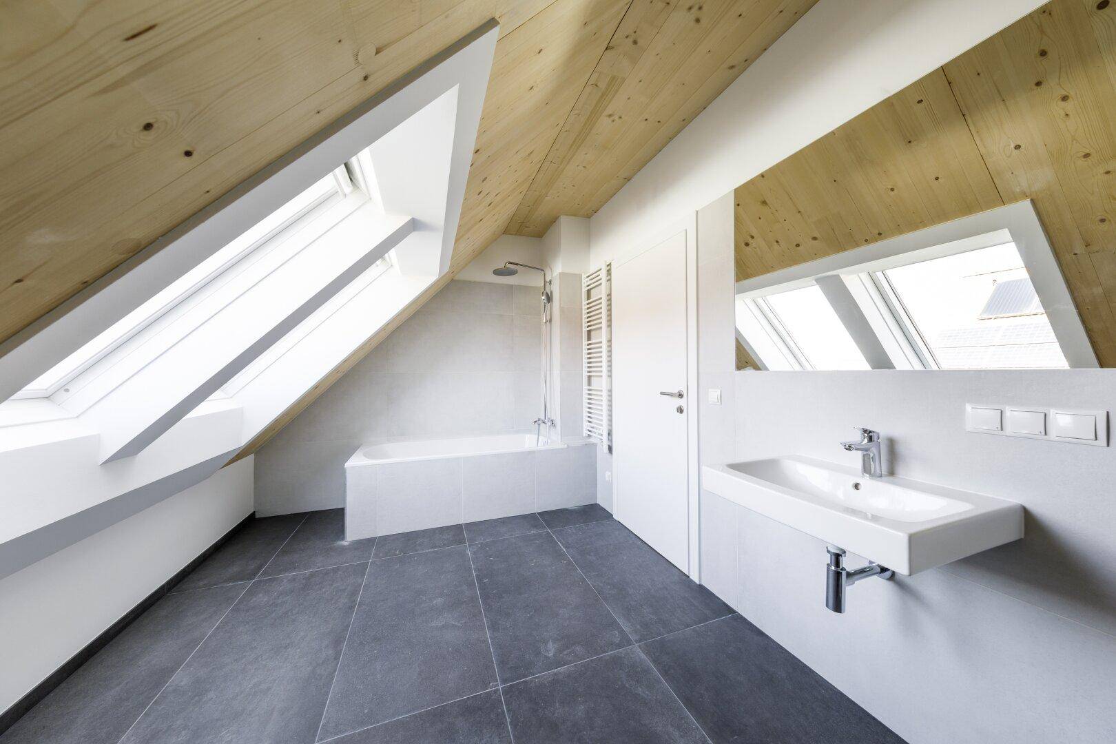 Modernes Badezimmer im Dachgeschoss mit Badewanne, Dusche und Dachfenstern.