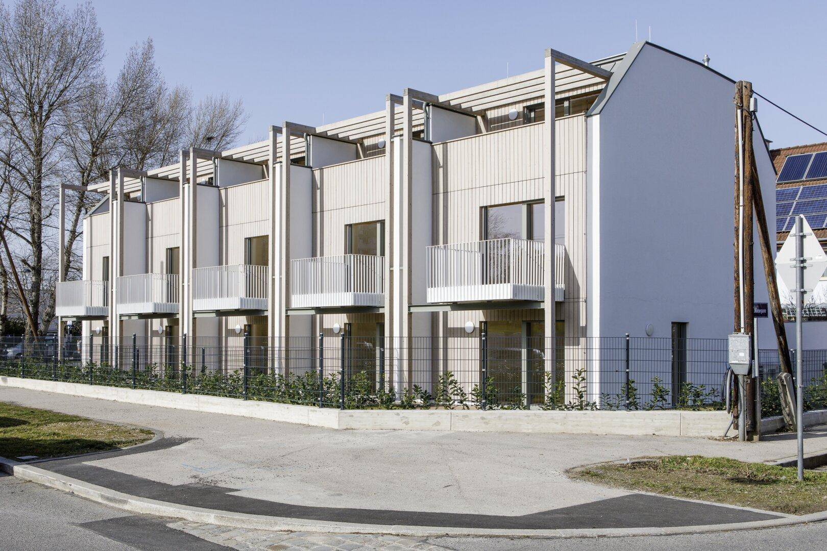 Moderne Reihenhäuser mit Holzfassade, Balkonen und Solaranlage auf dem Dach.