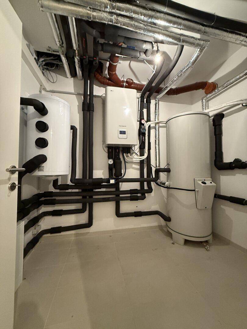 Technikraum im Keller mit Heizungsanlage, Warmwasserspeicher und Rohren.