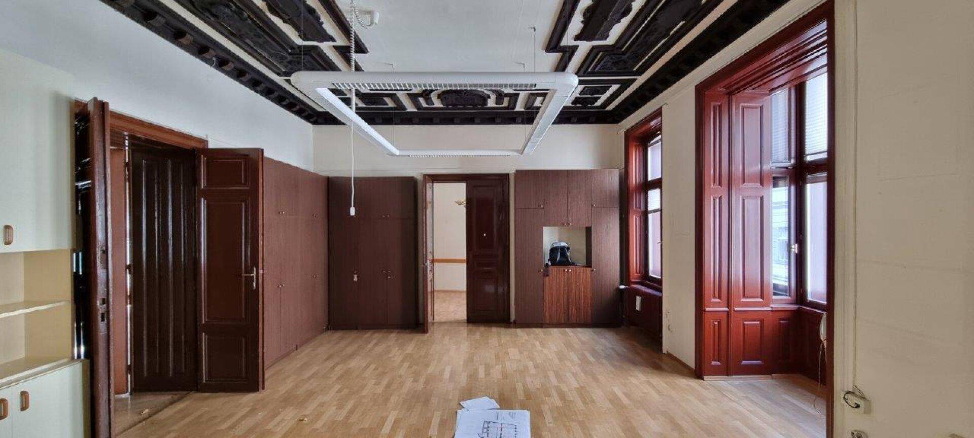 Geräumiger Wohnraum mit beeindruckender Holzkassettendecke, Parkettboden und hohen Fenstern.