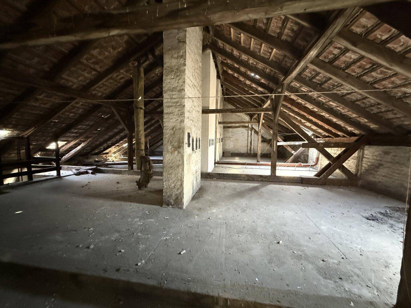 Geräumiger Dachboden mit sichtbaren Holzbalken und Ziegeln, bereit für den Ausbau.