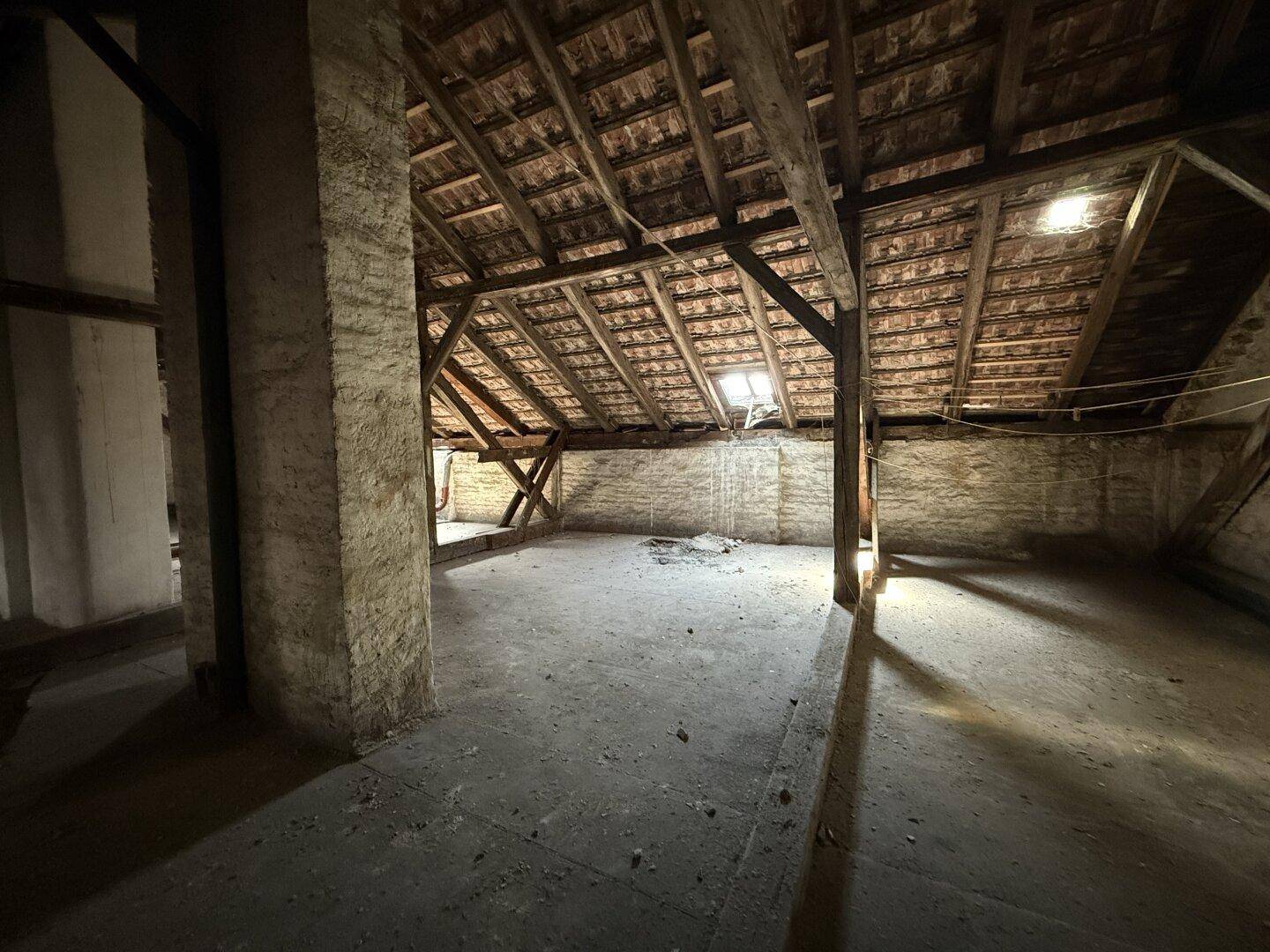 Dunkler Dachboden mit Holzbalken, Ziegeln und einem kleinen Dachfenster, das Licht spendet.