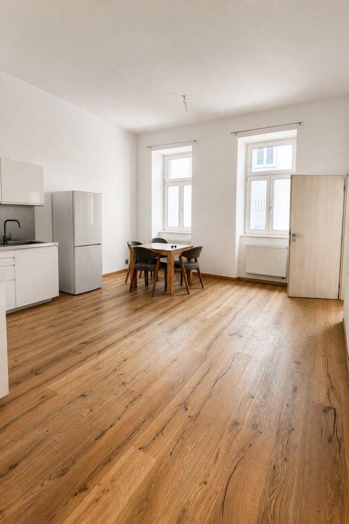 Heller Wohn- und Essbereich mit Holzboden, Esstisch und großen Fenstern, die viel Tageslicht hereinlassen.