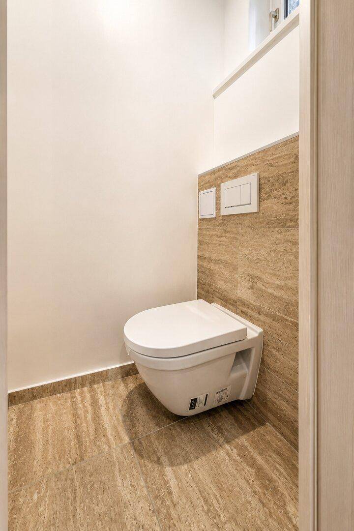 Modernes Gäste-WC mit wandhängender Toilette und beigefarbenen Fliesen an Wänden und Boden.