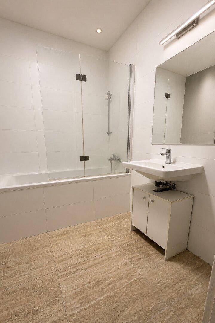 Helles Badezimmer mit Badewanne, Duschwand, modernem Waschbecken und beigefarbenen Fliesen.