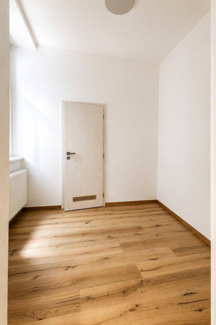 Unmöblierter Raum mit Holzboden und einem Fenster, das den Raum mit natürlichem Licht erfüllt.