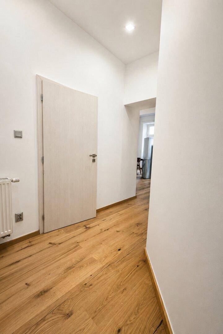 Heller Flur mit Holzboden und weißen Wänden, der zu weiteren Räumen der Wohnung führt.