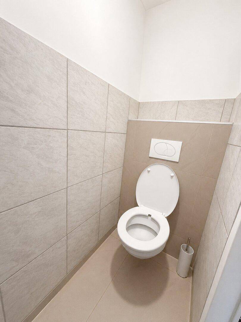 Separates WC mit wandhängender Toilette und beigefarbenen Fliesen an den Wänden.