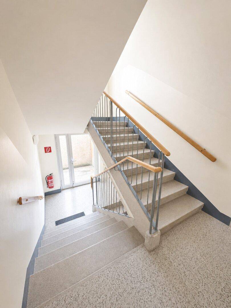 Helles Treppenhaus mit Terrazzoboden und Holzhandläufen, führt zu den oberen Etagen.