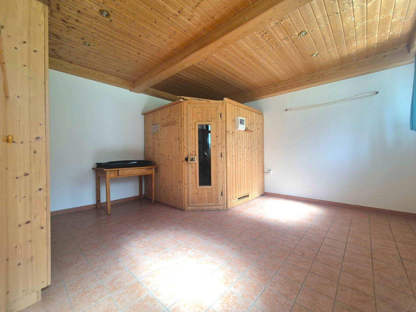 Raum mit einer holzvertäfelten Sauna, Fliesenboden und einer Holzdecke mit sichtbaren Balken.