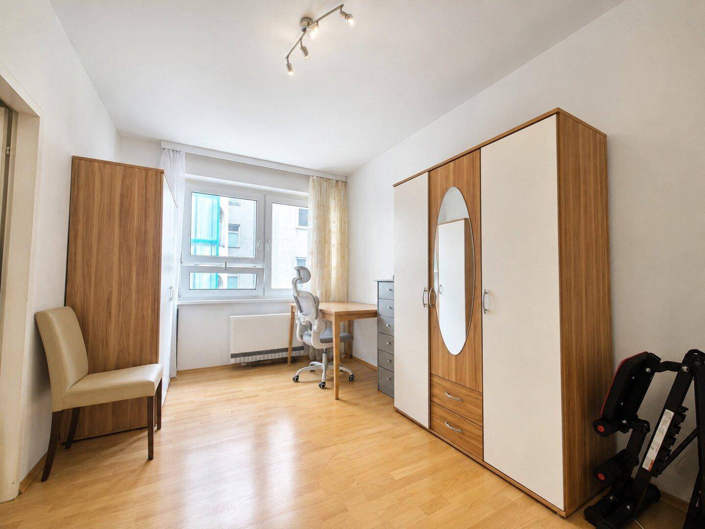Schlafzimmer mit Laminatboden, großem Kleiderschrank und einem Arbeitsbereich am Fenster.