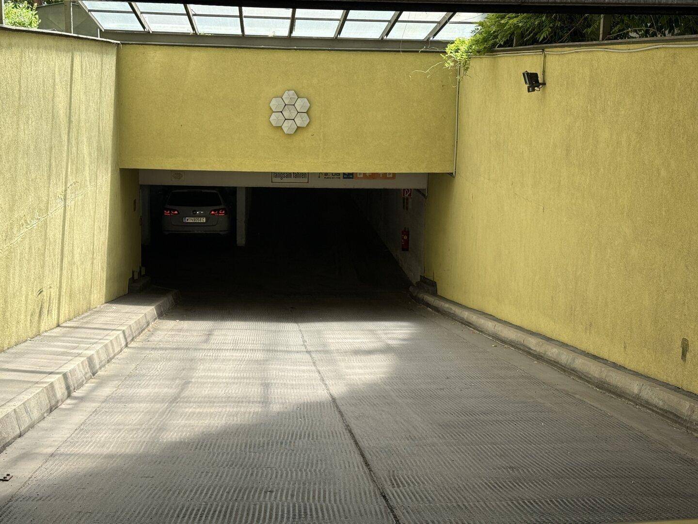 Eingangsbereich einer Tiefgarage mit gelber Fassade und Glasüberdachung, ein Fahrzeug ist im Tunnel sichtbar.